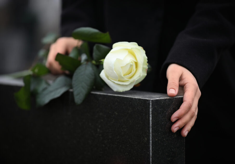 Woman,Holding,White,Rose,Near,Black,Granite,Tombstone,Outdoors,,Closeup.